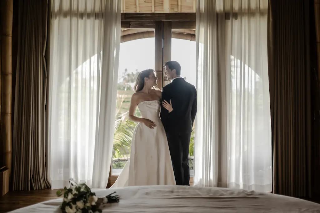 Couple by sheer-curtained villa windows looking out to the rice fields